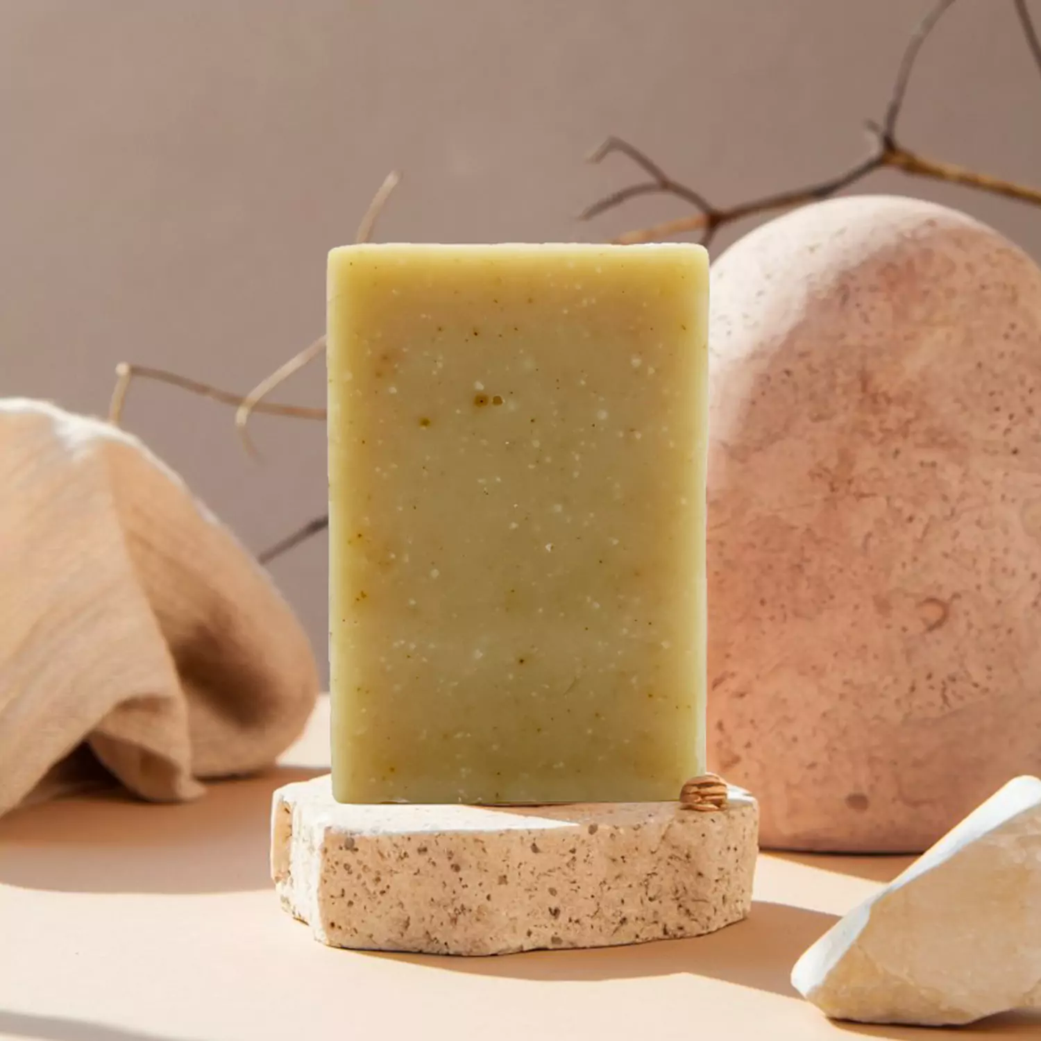Savon Monoï jaune clair avec petites inclusions, posé sur une tranche de pierre naturelle, décor minéral en arrière-plan.