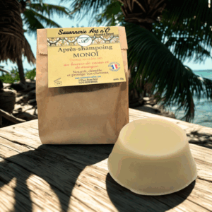 Après-shampoing solide Monoï sur une plage, emballage en papier kraft à côté, savon rond clair posé sur une planche en bois.