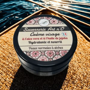 Crème visage au savonnerie Art n’O, pot noir étiqueté: aloe vera et huile de jojoba, hydratante légère pour peaux normales à sèches, photo en extérieur près de l’eau.