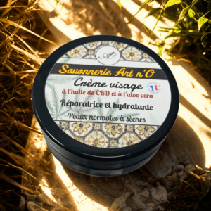 Crème visage biologique régénérante avec aloé vera, pot noir posé au sol dans un environnement végétal.