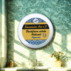 Dentifrice solide en galet citron menthe 100% bio et vegan posé sur un lavabo dans une salle de bain, étiquette jaune et bleue.