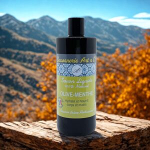 Savon liquide menthe-poivrée 500 ml en flacon noir, étiquette beige et bleu, montagne en arrière-plan et bois au premier plan.