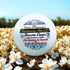 Baume corps Fleur d'oranger de 150 ml dans pot blanc aluminium au milieu de fleurs blanches en champ, étiquette bleue et dorée visible.
