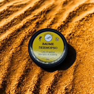 Petit pot de Baume Dermopsо sur sable doré, label jaune et noir indiquant confort apaisant pour psoriasis et eczéma.