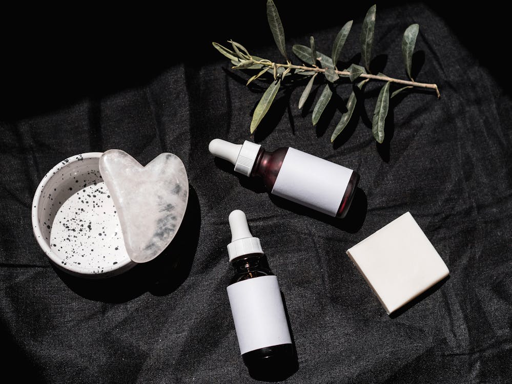 Flacons compte‑gouttes en verre et petites bouteilles d’apothicaire sur fond sombre, évoquant huiles essentielles et préparations naturelles pour le soin du visage