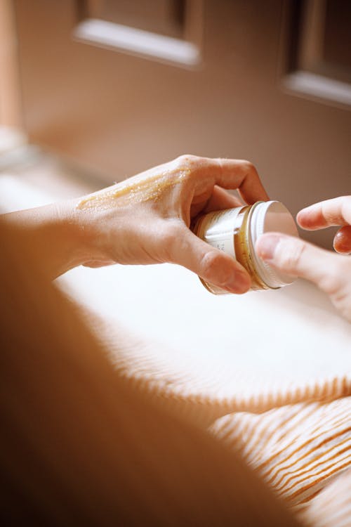 Pot de baume naturel pour la peau posé en lumière douce, texture onctueuse et application au doigt, suggérant un soin artisanal et apaisant pour la peau