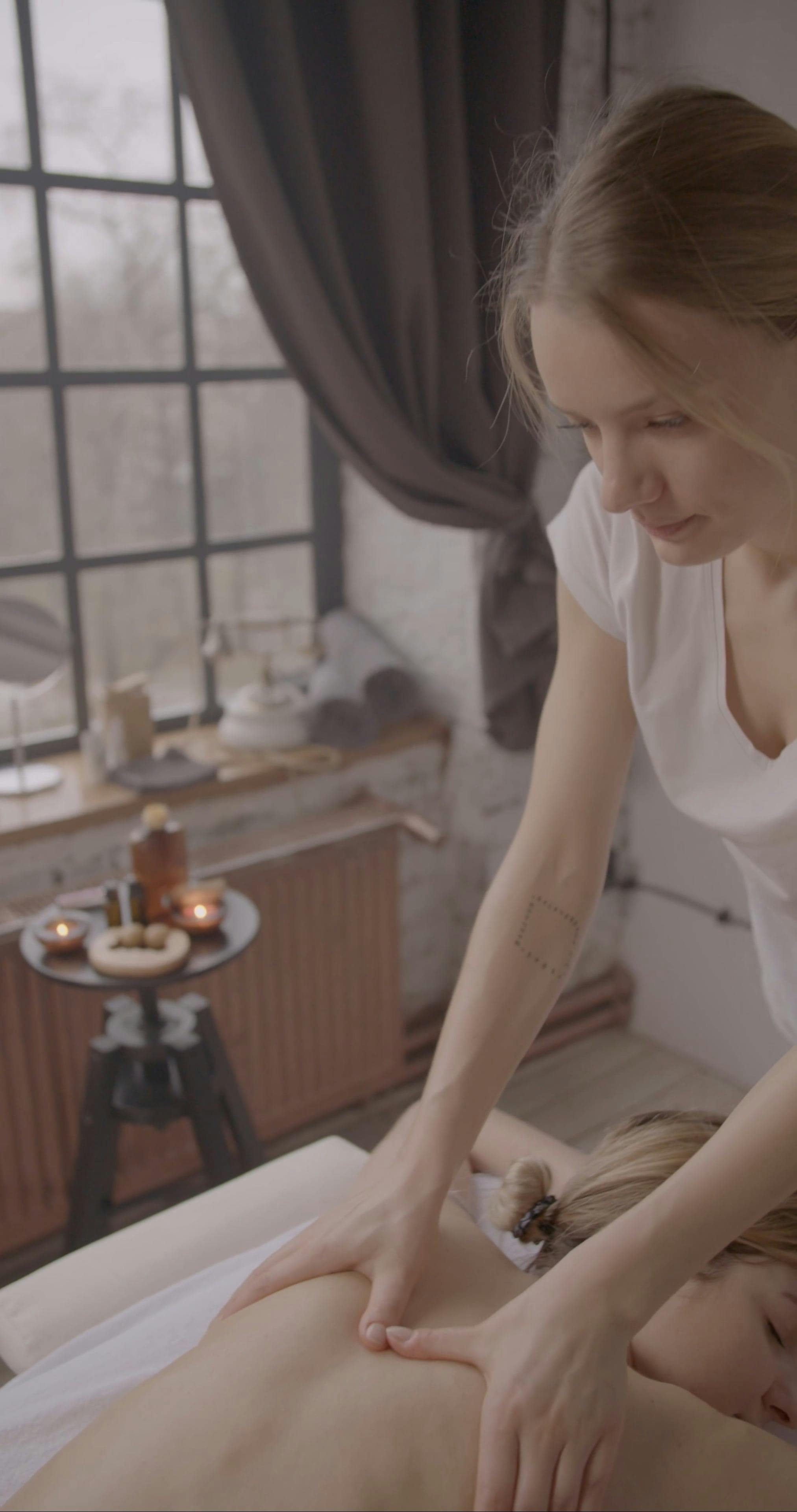 Massage des épaules et du dos dans un spa à la lumière naturelle, en surplomb avec bougies et huiles essentielles.