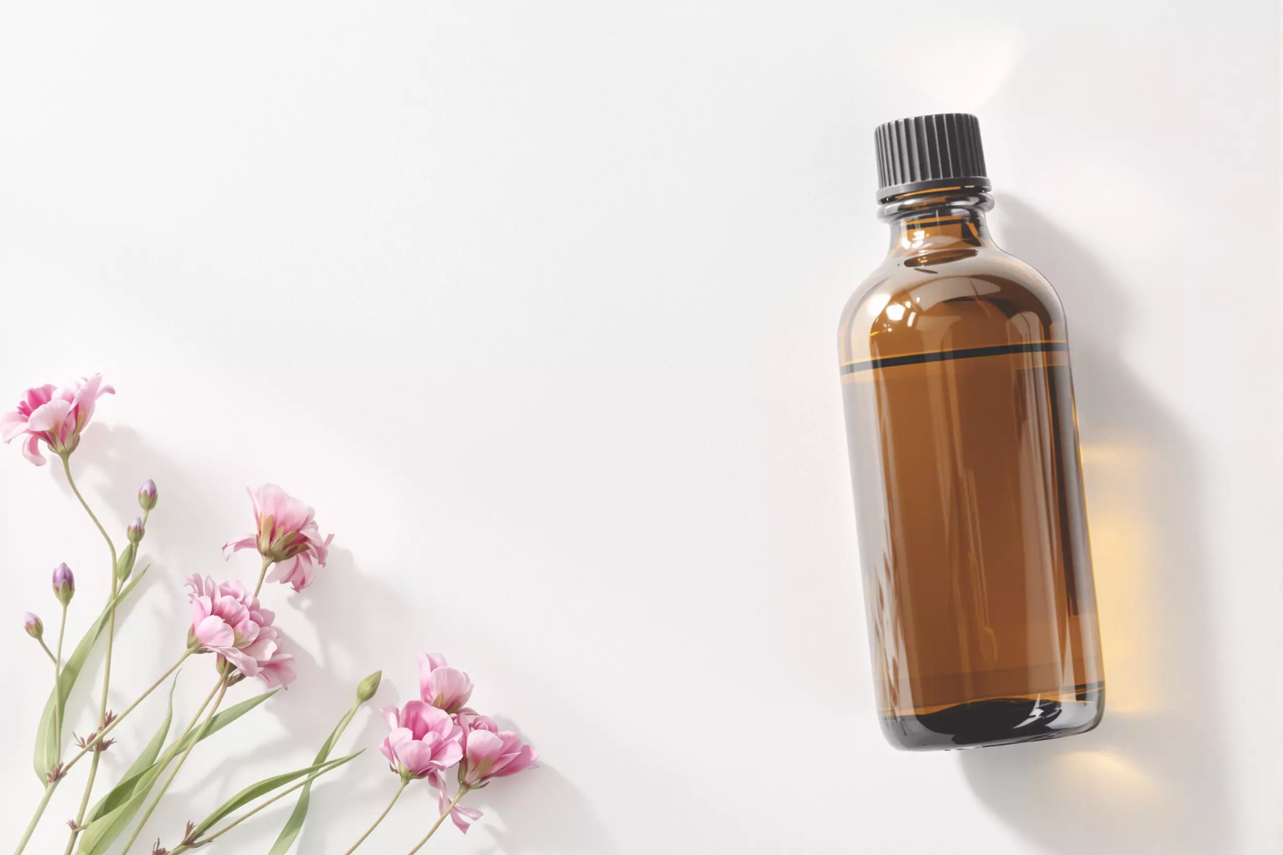 Flacon en verre ambré avec compte-gueules et fleurs roses (huiles essentielles) sur fond blanc.