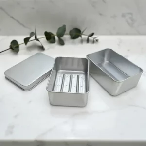 Boîte de transport savon en métal argenté avec séparateur amovible, plaque inférieure perforée, couvercle posé à côté sur plan marbre.