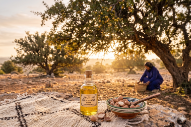 bouteille d'huile d'argan sur un tapi avec une femme qui récolte des fruits