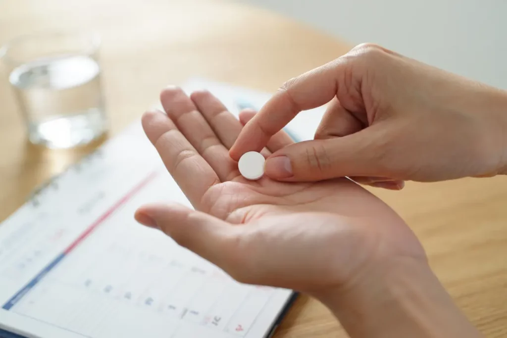 Pilule blanche entre les doigts, sur fond de papier et verre d’eau, évoquant un nouveau traitement psoriasis 2025 et ses avancées.