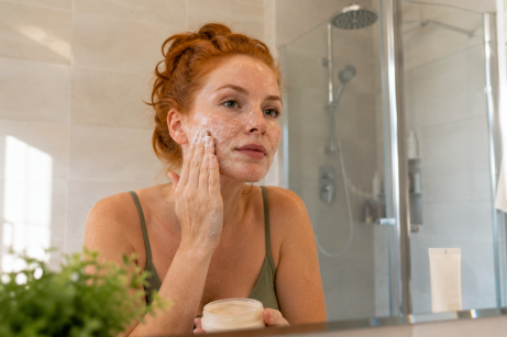 routine skincare peau acnéique. Une femme rousse dans sa salle de bain qui nettoie son visage avec de l'acné